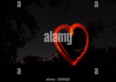 Cœur rouge sur fond noir de nuit. Coeur dessiné par le feu sur fond sombre. Amour, romantique et concept de festival Banque D'Images