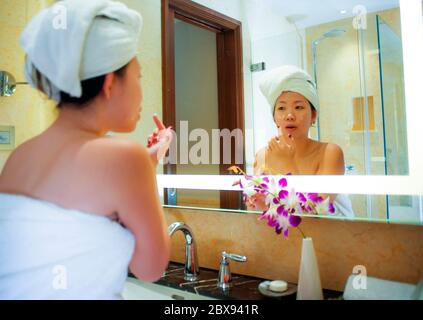 Style de vie portrait frais de jeune bonne et belle femme coréenne asiatique à la maison ou à l'hôtel salle de bains enveloppé dans serviette de toilette appliquant le maquillage gai an Banque D'Images