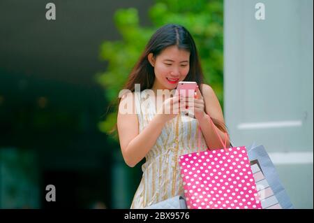 Portrait de style de vie de jeune femme chinoise asiatique heureuse et belle marchant dans la rue portant des sacs d'achats en utilisant le téléphone portable recherche en ligne f Banque D'Images