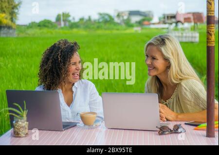 deux amies joyeuses travaillant à l'extérieur dans un beau café internet avec ordinateur portable, une femme caucasienne et une fille afro mixte d'ethnie enjoyin Banque D'Images