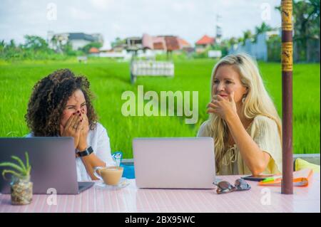 deux amies joyeuses travaillant à l'extérieur dans un beau café internet avec ordinateur portable, une femme caucasienne et une fille afro mixte d'ethnie enjoyin Banque D'Images