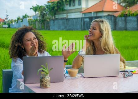 deux amies joyeuses travaillant à l'extérieur dans un beau café internet avec ordinateur portable, une femme caucasienne et une fille afro mixte d'ethnie enjoyin Banque D'Images