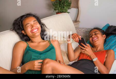 Jeunes belles et heureuses amies asiatiques couple ou sœurs appréciant Internet médias sociaux s'amuser avec le téléphone portable à la maison canapé canapé Banque D'Images