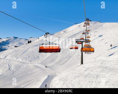 Télésiège avec abri à bulles orange le jour d'hiver ensoleillé. Neige blanche et ciel bleu clair à Saalbach Hinterglemm Leogang Resort, Autriche, Alpes, Europe. Banque D'Images