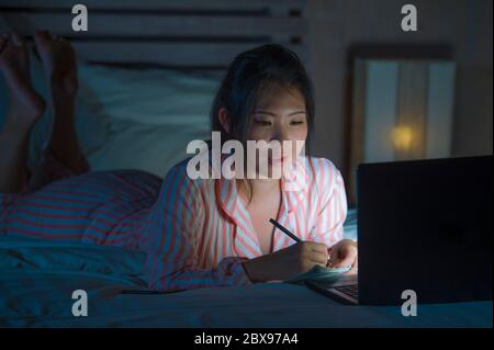 Jeune fille étudiante asiatique coréenne, belle et confiante, recherchant et étudiant à la maison, préparant l'examen avec ordinateur portable sur lit écrivant tard à ni Banque D'Images