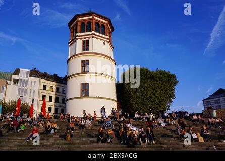 La tour historique „Schlossturm (château) de la vieille ville de Düsseldorf avec des personnes assises sur les marches et profitant du soleil. Banque D'Images