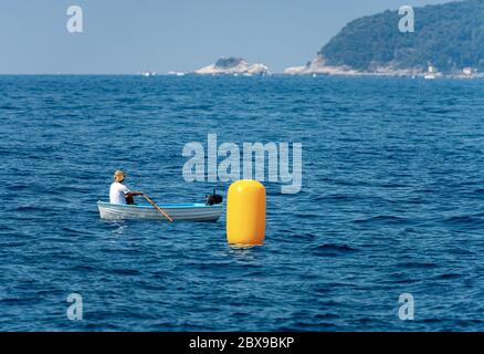 Un homme avec un chapeau de paille au milieu de la mer, se rogue sur un petit bateau à côté d'une grande bouée jaune. Golfe de la Spezia, Ligurie, Italie Banque D'Images