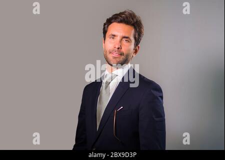 jeune homme heureux élégant et beau en costume posant pour entreprise portrait d'affaires détendu et confiant sourire heureux isolé sur gris comme su Banque D'Images