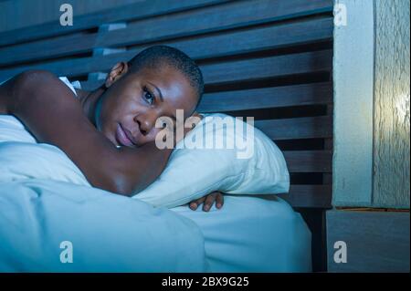 Jeune triste et déprimé noir afro américaine femme dans le lit sans sommeil tard la nuit se sentant désespéré regardant inquiet et anxieux souffrant dépression probl Banque D'Images