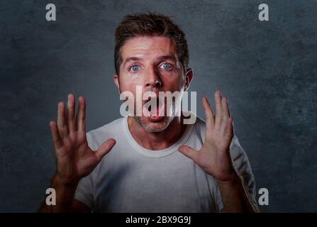 Portrait de jeune homme caucasien attrayant en état de choc et surpris les mains montantes émerveillées et alarmées avec la bouche et les yeux largement ouverts dans l'incrédulité et la surpeur Banque D'Images