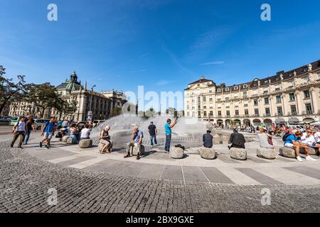 Les touristes visitent la Karlsplatz ou Stachus, grande place, dans le centre de Munich avec une fontaine, en arrière-plan le Palais de Justice (Justizpalast), Allemagne Banque D'Images