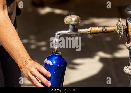 Gros plan d'une main de femme tout en remplissant une bouteille d'eau d'un robinet lors d'une chaude journée d'été. Italie, Europe Banque D'Images