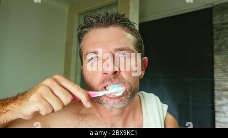 portrait de style de vie domestique de jeune beau et attrayant homme avec les yeux bleus à la maison salle de bains avec une serviette sur l'épaule lavage des dents avec brosse à dents Banque D'Images