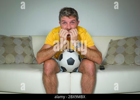 jeune supporter de football excité et nerveux homme regardant le match de football à la télévision dans le salon canapé piquant les ongles sentant l'émotion folle et s Banque D'Images