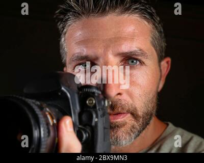 gros plan portrait d'un homme beau et attrayant sur son 30d tenant un appareil photo reflex professionnel à côté de son visage isolé sur fond noir dans Banque D'Images