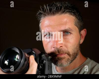 gros plan portrait d'un homme beau et attrayant sur son 30d tenant un appareil photo reflex professionnel à côté de son visage isolé sur fond noir dans Banque D'Images