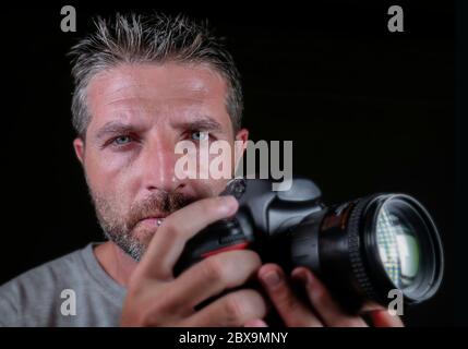 gros plan portrait d'un homme beau et attrayant sur son 30d tenant un appareil photo reflex professionnel à côté de son visage isolé sur fond noir dans Banque D'Images