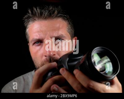 gros plan portrait d'un homme beau et attrayant sur son 30d tenant un appareil photo reflex professionnel à côté de son visage isolé sur fond noir dans Banque D'Images