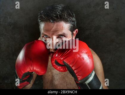 jeune homme de sport en colère et féroce en gants de boxe posant dans badass fighter attitude cool et furieux dans la position de boxer isolé sur fond noir en d Banque D'Images