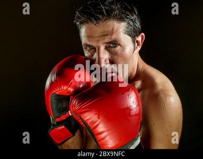 jeune homme de sport en colère et féroce en gants de boxe posant dans badass fighter attitude cool et furieux dans la position de boxer isolé sur fond noir en d Banque D'Images