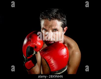 jeune homme de sport en colère et féroce en gants de boxe posant dans badass fighter attitude cool et furieux dans la position de boxer isolé sur fond noir en d Banque D'Images