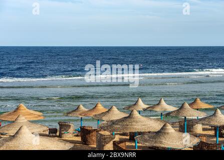 Plage de la mer Rouge avec parasols en paille près de Marsa Alam, Egypte, Afrique. Les vagues de la mer se sont écrachées sur le récif de corail Banque D'Images