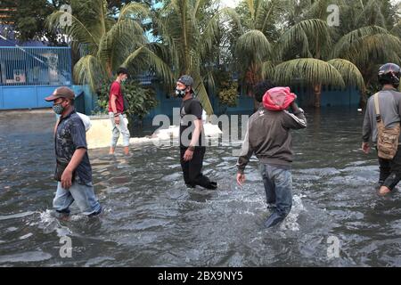 Jakarta, Indonésie. 06e juin 2020. Des hommes portant des masques faciaux sont vus marcher dans une rue inondée de rob à Jakarta.Rob inondations à Jarkata, c'est un phénomène où l'eau de mer déborde dans le continent. Il peut également être interprété comme une flaque d'eau sur les terres côtières qui se produit lorsque les eaux de marée sont élevées ainsi inundate parties de la plaine côtière. Crédit : SOPA Images Limited/Alamy Live News Banque D'Images