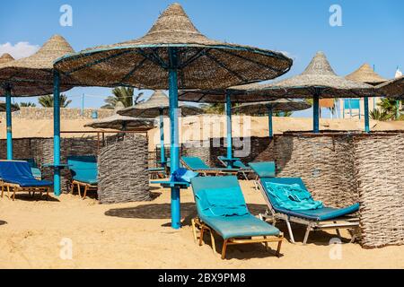 Groupe de parasols en paille et de transats dans une plage de sable de la mer Rouge, station touristique près de Marsa Alam, Egypte, Afrique Banque D'Images