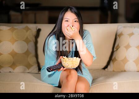 Jeune femme asiatique, belle et effrayée, adolescente chinoise dans la peur, regardant un film effrayant à la maison canapé canapé canapé canapé, mangeant un bol de pop-corn tenant la télécommande cont Banque D'Images