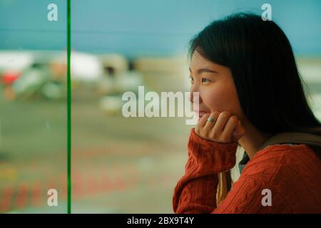 Jeune femme étudiante chinoise asiatique heureuse et excitée avec sac à dos dans le salon de départ de l'aéroport, regardant l'avion à travers une fenêtre en verre souriant prêt à l'emploi Banque D'Images