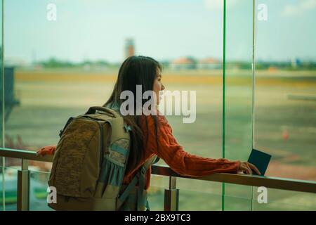 Jeune femme étudiante chinoise asiatique heureuse et excitée avec sac à dos dans le salon de départ de l'aéroport, regardant l'avion à travers une fenêtre en verre souriant prêt à l'emploi Banque D'Images