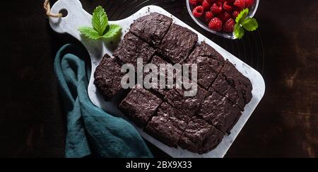 bannière de tarte au chocolat au brownie végétalien avec tahini et framboises fraîches sur fond sombre Banque D'Images