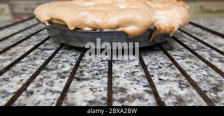 Tarte au citron meringue dans un moule reposant sur un plateau de refroidissement sur un plan de travail en granit Banque D'Images