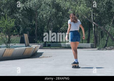 Une jeune fille fait du skateboard dans le parc. Par temps ensoleillé, par une chaude journée d'été. Banque D'Images