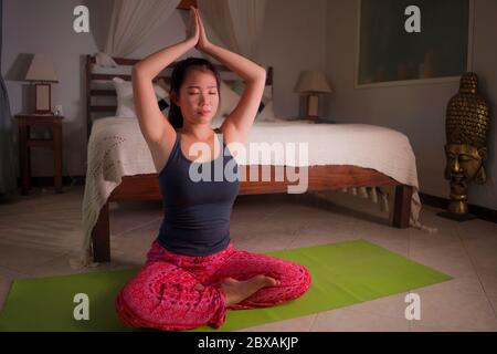 Jeune femme coréenne asiatique heureuse et belle à la maison chambre à coucher faire l'entraînement de méditation sur le tapis de yoga détendu et paisible dans le bien-être et la vie saine Banque D'Images