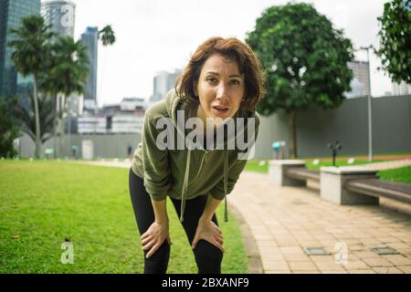 portrait extérieur de jeune femme attirante, fatiguée et respirante de jogging épuisé après l'entraînement de course dans le magnifique parc de la ville en forme Banque D'Images