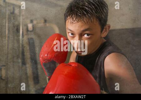 un jeune garçon dur et frais qui frappe sur un sac lourd . 13 ou 14 ans asiatique adolescent entraînement Thai boxe entraînement regardant défi comme un badass de combat pr Banque D'Images