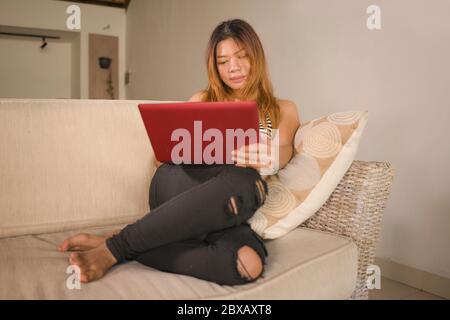 Jeune femme asiatique indonésienne belle et attrayante en Jean et décontracté haut à la maison travaillant détendu et heureux avec ordinateur portable de réseautage utilisant Banque D'Images