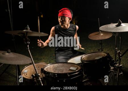 Asiatique américain mixte adolescent jouant des tambours à la maison jardin . cool et beau jeune garçon pratiquant sur le kit de tambour répéter passionné dans badass rock b. Banque D'Images