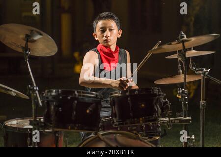 jeune garçon comme batteur de groupe de rock talentueux . Beau et cool adolescent d'Amérique asiatique jouant tambour installé dans le jardin de la maison imitant la musique de nuit comme hobb Banque D'Images