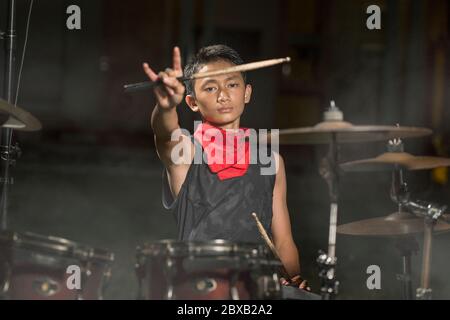 jeune garçon comme batteur de groupe de rock talentueux . Beau et cool adolescent d'Amérique asiatique jouant tambour installé dans le jardin de la maison imitant la musique de nuit comme hobb Banque D'Images