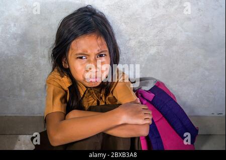 portrait dramatique de triste et déprimé de 8 ou 9 ans enfant en uniforme d'école assis sur le sol avec ses mauvaises pleurs se sentant effrayés et d Banque D'Images