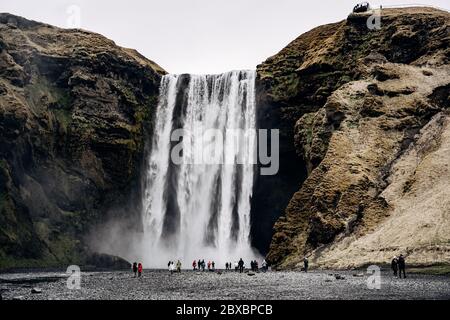 Cascade de Skogafoss dans le sud de l'Islande, sur l'anneau doré. Les visiteurs sont venus voir la cascade, les touristes marchent au pied de la montagne. Banque D'Images