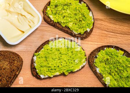 Planche en bois avec sandwichs avocat, pain et un paquet ouvert de fromage à la crème. Plat végétarien. Vue de dessus d'une mise en page à plat. Banque D'Images