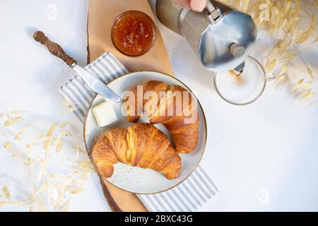 Petit déjeuner continental, une tasse de café avec lait, deux croissants sur une plaque en céramique avec beurre et confiture d'orange sur une planche à rameet en bois, vue de a Banque D'Images