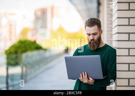 Beau barbu homme tenant et utilisant un ordinateur portable dans la rue de la ville