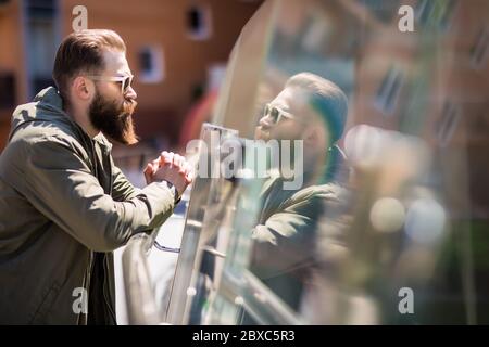 Beau barbu homme dans des lunettes de soleil regarde la caméra en se tenant sur le balcon Banque D'Images