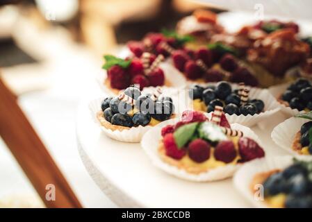 Délicieux petits gâteaux servis sur les plateaux du buffet. Petits gâteaux aux framboises et aux myrtilles. Desserts à la fête. Célébration, fête, anniversaire ou mariage Banque D'Images