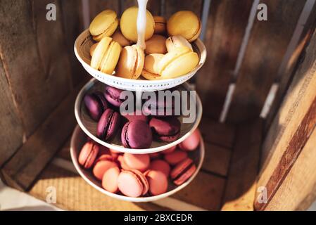 Assiette à trois niveaux avec macarons doux colorés. Fond de la boîte en bois. Dessert servi avec thé ou café l'après-midi. Mariage ou fête Banque D'Images