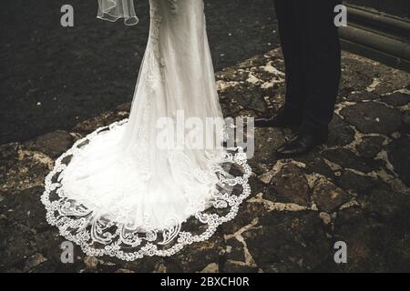 Gros plan des jambes de couple de mariage. Mariée en dentelle blanche robe de mariage avec longue piste sur sol pavé de pierre. Concept de mariage. Banque D'Images